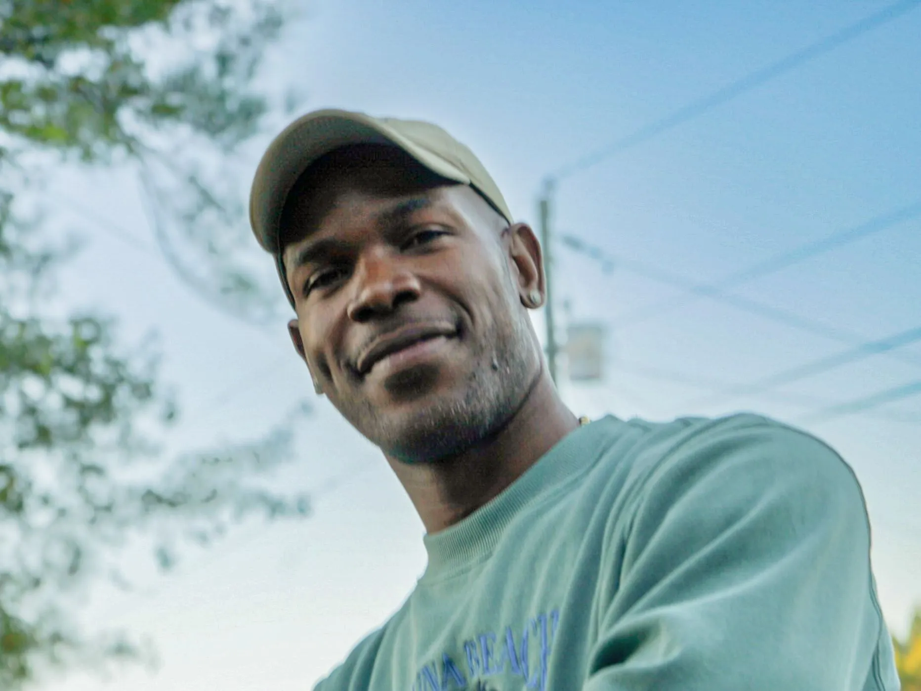 a man in a green shirt and hat holding a cell