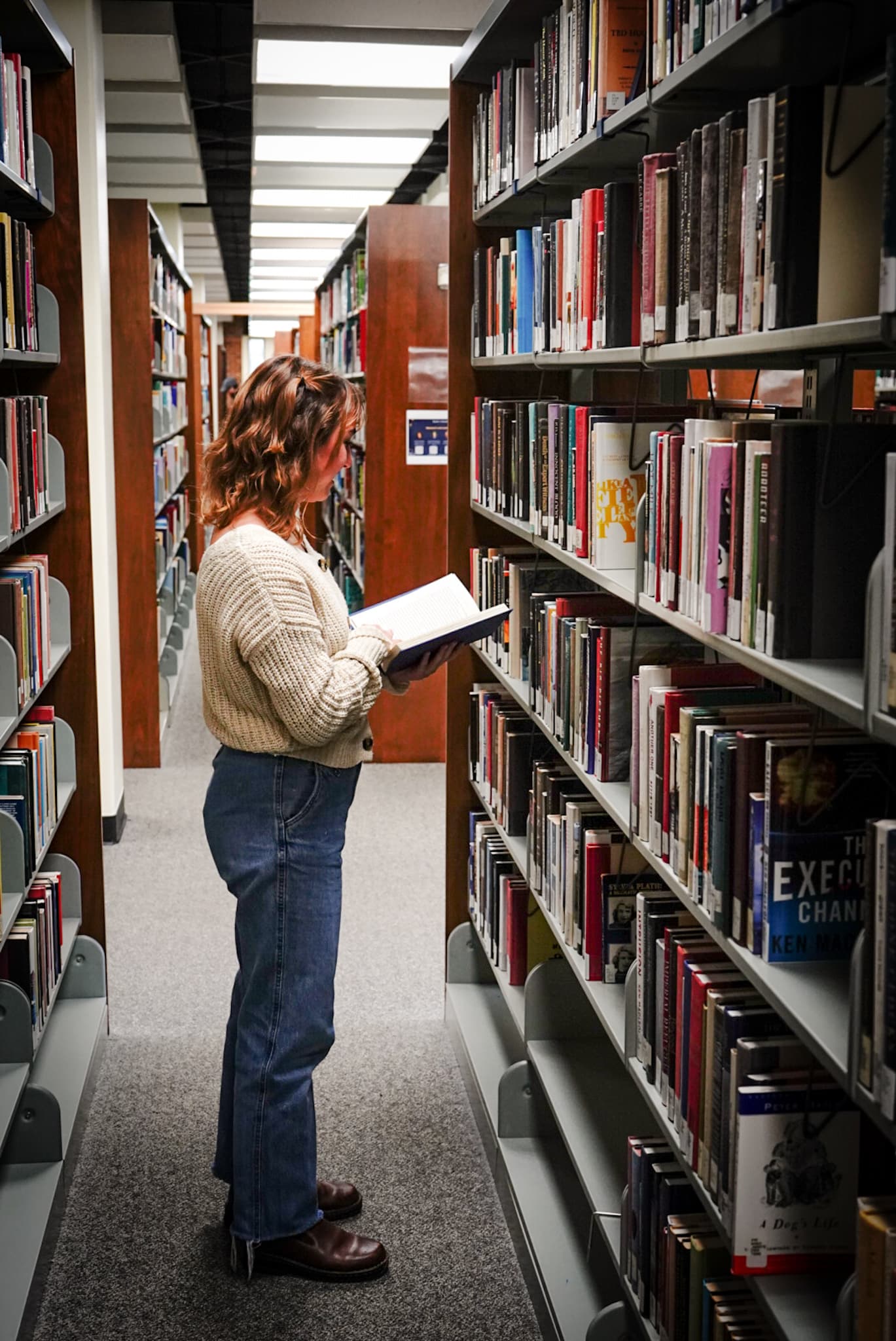 a woman standing in a library reading a book