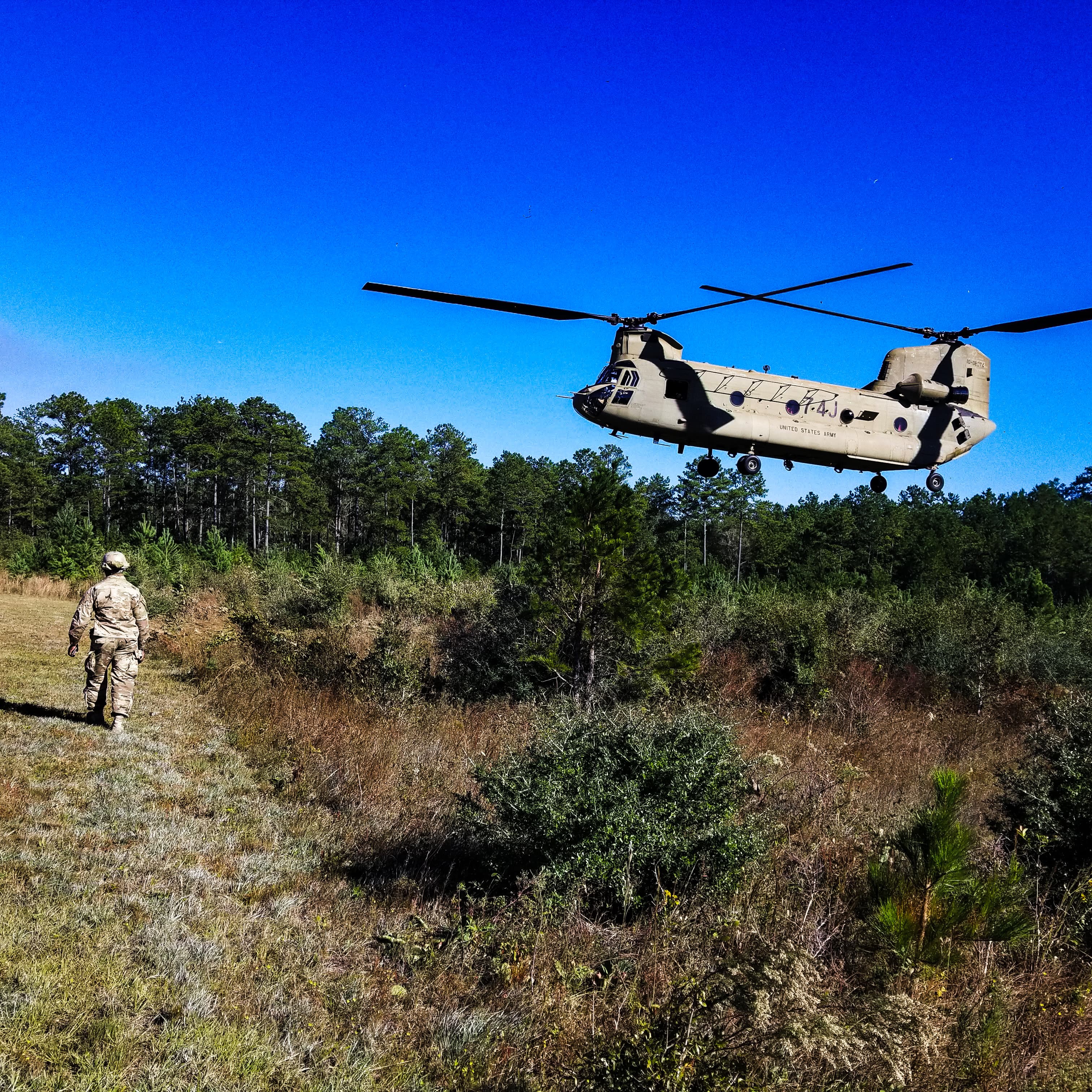 a military helicopter flying over a field with a man