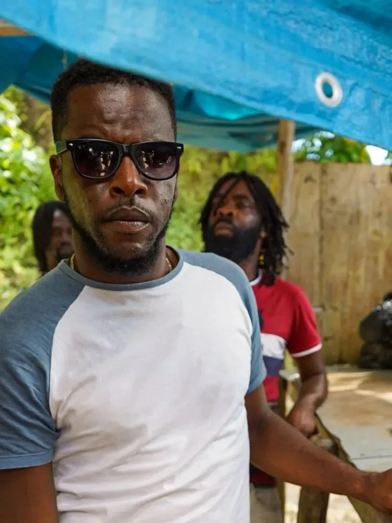 a man in sunglasses and a white shirt stands outside